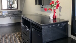 A modern kitchen with a black countertop, a built-in oven, and a microwave. There is a small table with a vase of red flowers. - Villa Inn & Suites (Inglewood)