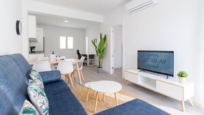 Un salon moderne comprenant un canapé, une table à manger, des chaises, un téléviseur et une plante en pot.