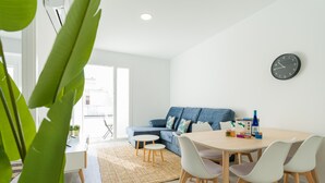 Un salon moderne avec un canapé, une table à manger et des chaises, une horloge au mur et une grande plante.