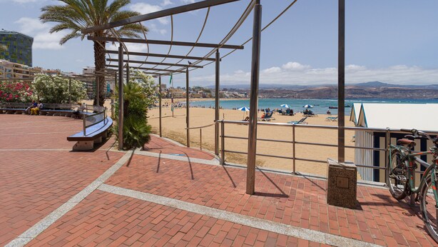 Une promenade en bord de mer agrémentée d’une pergola en métal, de bancs et d’un vélo.
