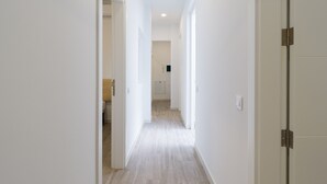 A narrow hallway with white walls and light wood flooring, leading to a bathroom and a kitchen area. - Volcano La Colorada By CanariasGetaway (Las Palmas de Gran Canaria)