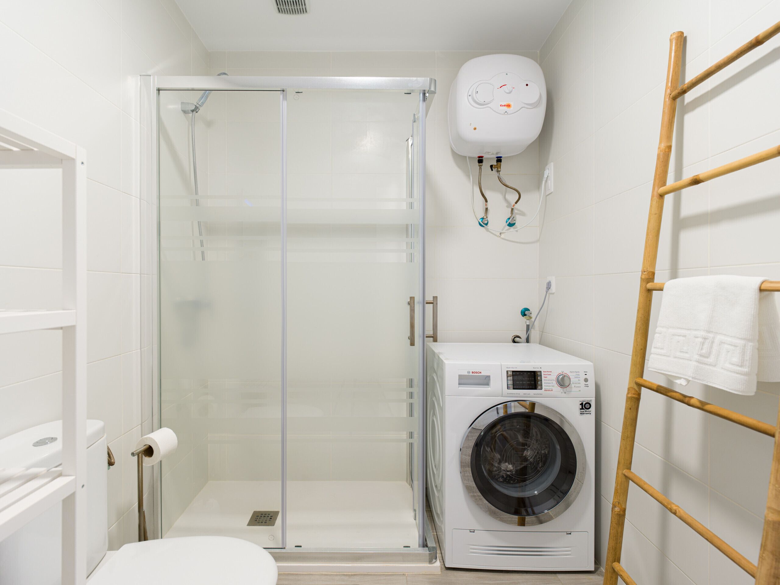 A compact bathroom with a glass shower enclosure, a Bosch washing machine, and a towel rack.