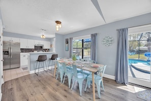 Een moderne keuken met een eethoek, grote ramen en uitzicht op een zwembad.