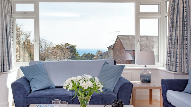 Een woonkamer met een bank, een bijzettafel met een bloevas, een schaal fruit en uitzicht op de zee.