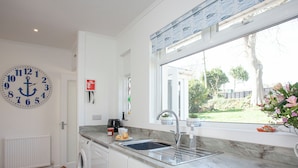 Een moderne keuken met een grote klok, een wasmachine, een spoelbak en een raam met uitzicht op de tuin.