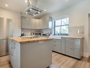Een moderne keuken met een centraal eiland, inbouwapparatuur en een raam dat voor daglicht zorgt.