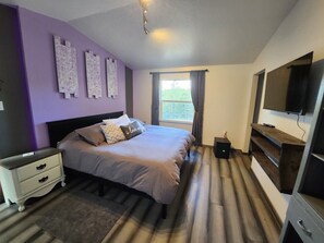 Quarto com cama, mesa de cabeceira, televisão e janela com cortinas.