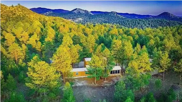 Una cabana envoltada de bosc amb muntanyes al fons.