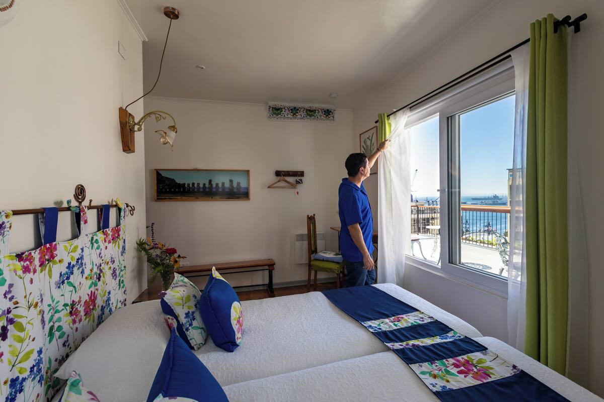 A bedroom with a bed, a window, a painting, and a chair.