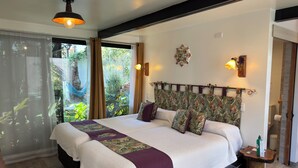 A large bed with a floral headboard, a bedside table with a green bottle, and a view of greenery outside. - AYCA La Flora Hotel Boutique (Valparaiso)