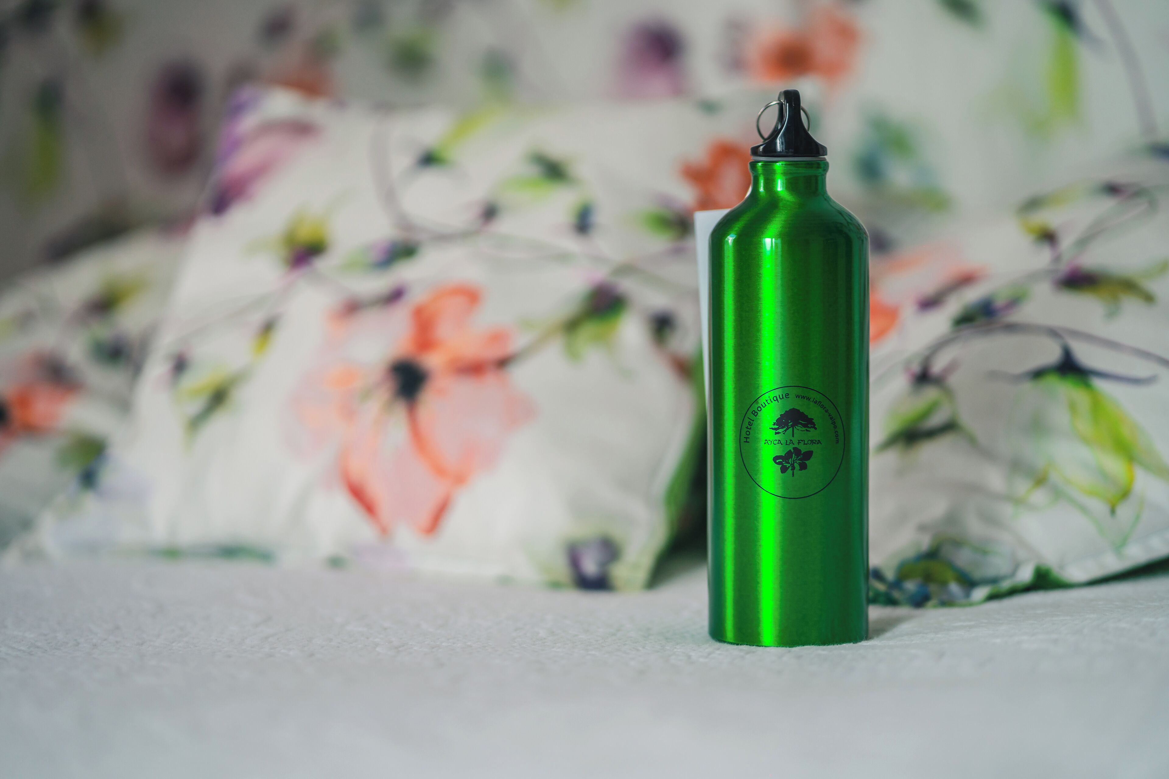 A green water bottle with a label on a floral-patterned fabric background.