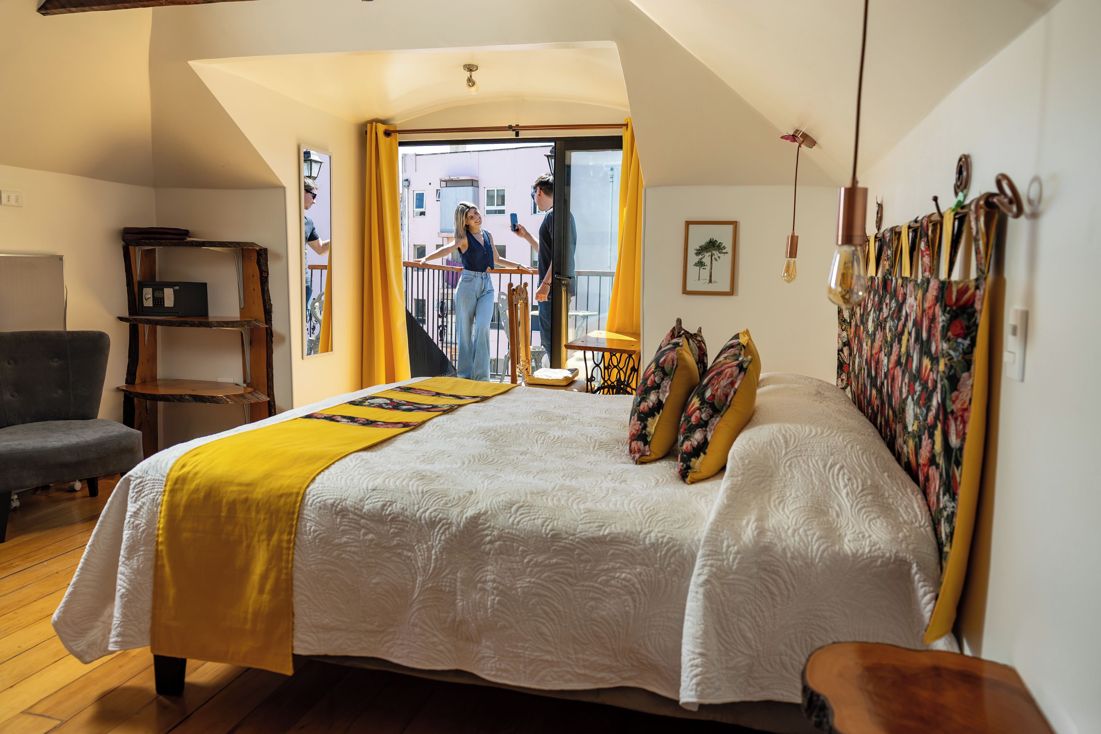 Une chambre avec un grand lit, une chaise en bois, une petite table, un balcon avec vue et un ventilateur de plafond.