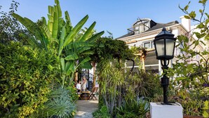 Un sendero en un jardín que conduce a un edificio con balcón, rodeado de abundante vegetación y un farol.