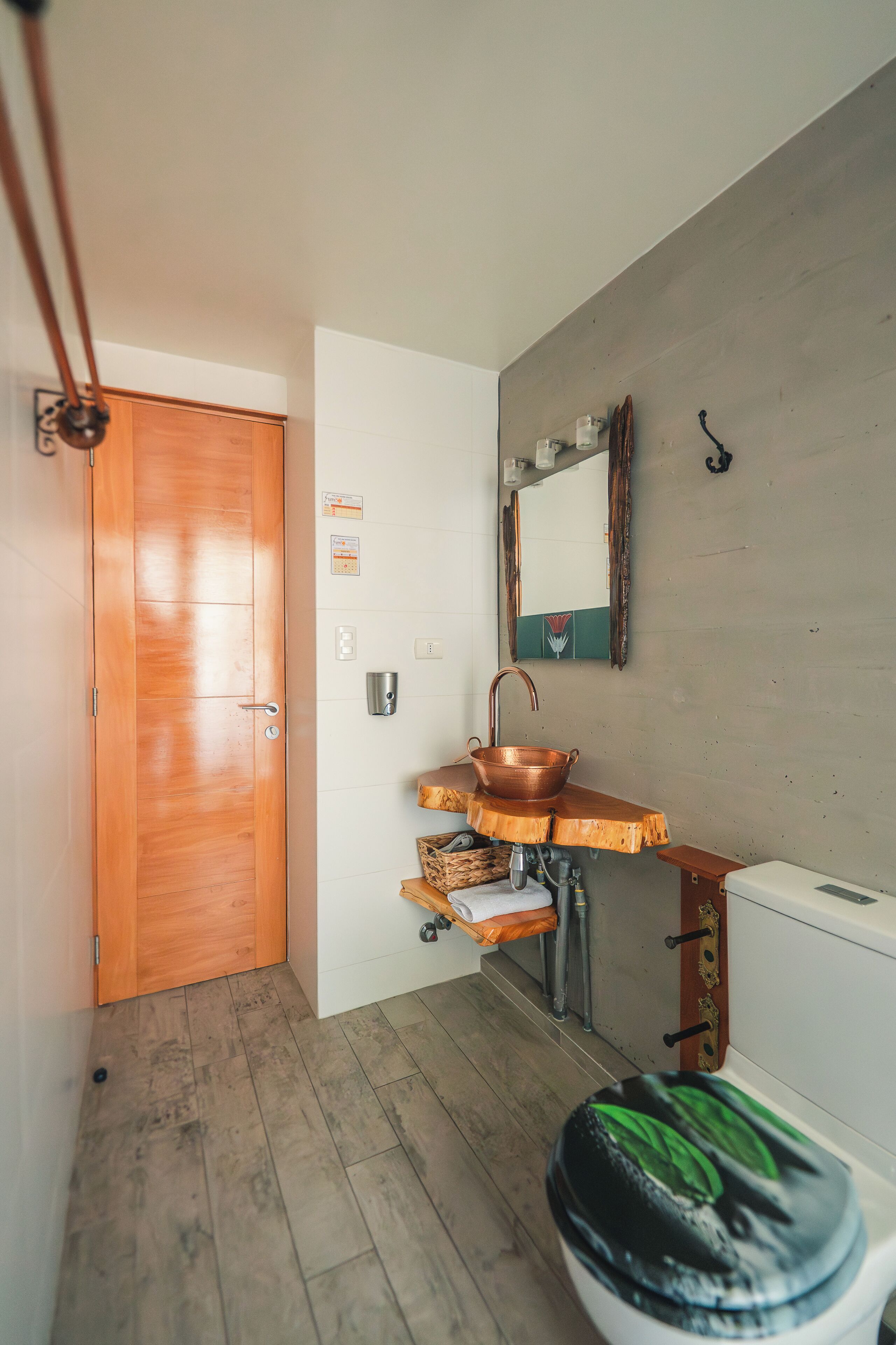 Een badkamer met een houten deur, een koperen wastafel, een spiegel en een toilet.