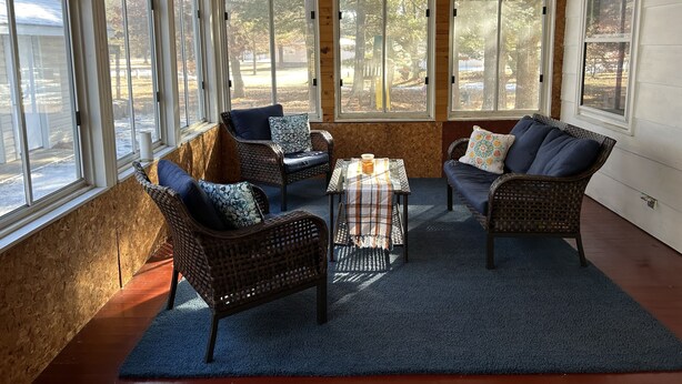 A sunroom with wicker furniture, large windows, and a ceiling fan.