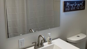 A bathroom with a white sink, a mirror, and a sign that says "Please be sweet and wipe the seat."