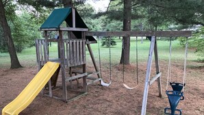 A wooden playground with a slide and swings.