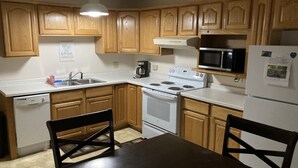 A kitchen with wooden cabinets, a white stove, a microwave, and a refrigerator.