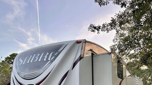 Una caravana Sabre estacionada al aire libre, con una sección trasera visible que incluye un área de ducha extraíble y un pequeño espacio para la cocina.