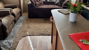 Interior acogedor de una autocaravana con sofá, una pequeña cocina y ventana que deja entrar luz natural.