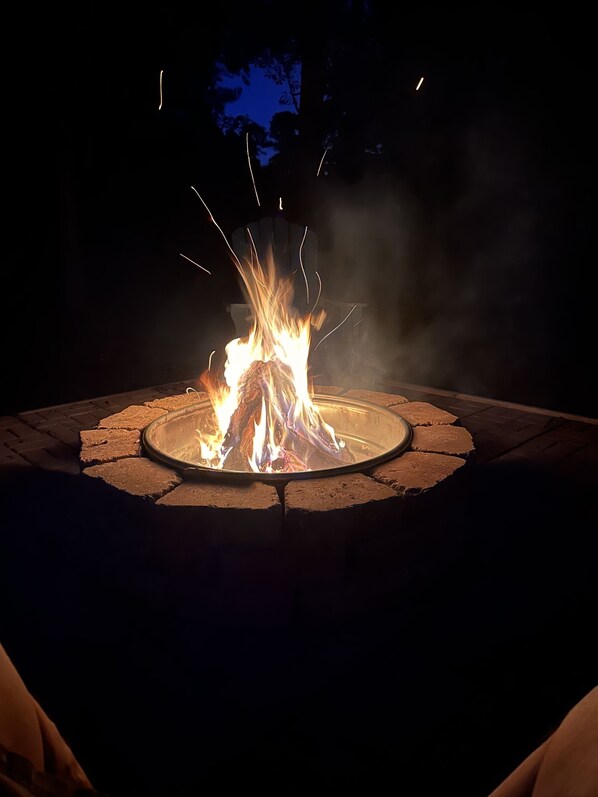 A circular fire pit with a metal rim, surrounded by a brick border, set in an outdoor area.