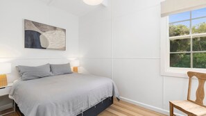 A bedroom with a bed, bedside lamps, a window with a view, and a painting on the wall.