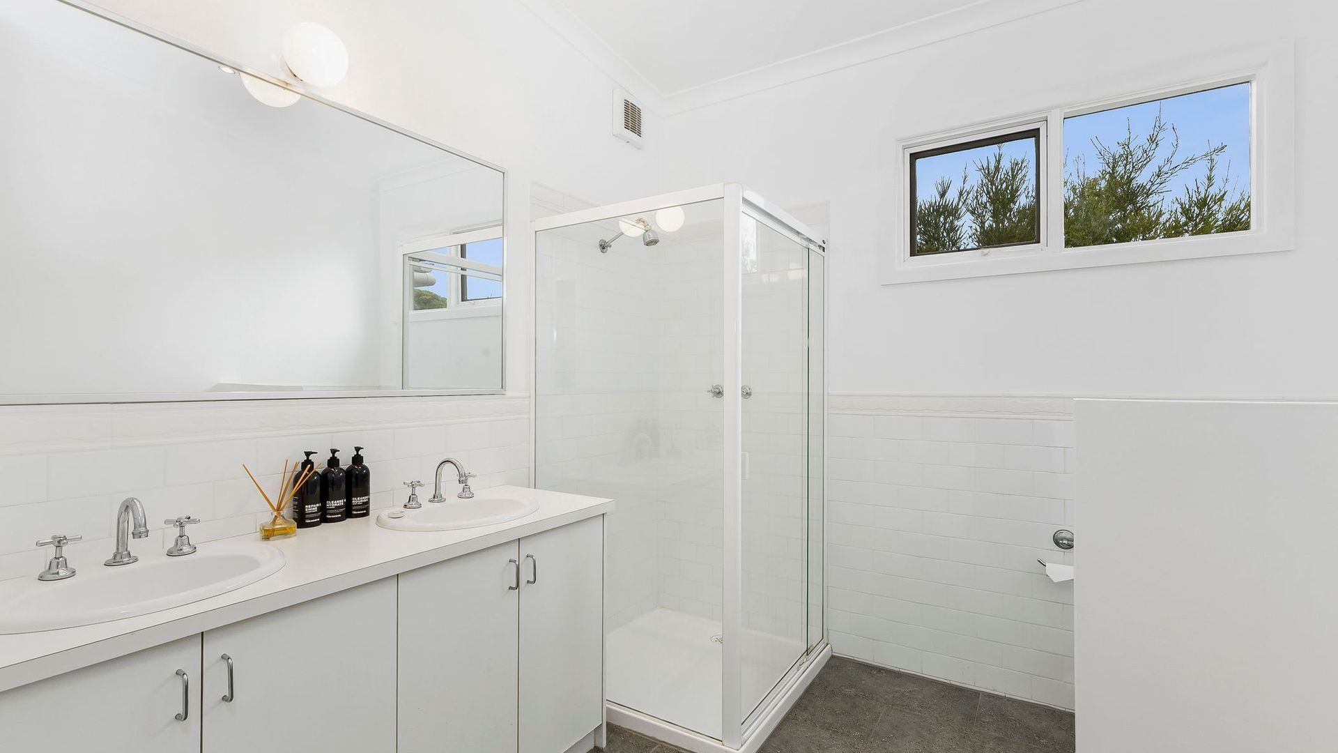 Ein modernes Badezimmer mit großem Spiegel, Duschkabine und Fenster mit Blick auf Bäume.