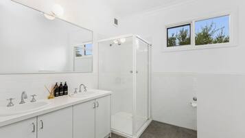 Ein modernes Badezimmer mit großem Spiegel, Duschkabine und Fenster mit Blick auf Bäume.
