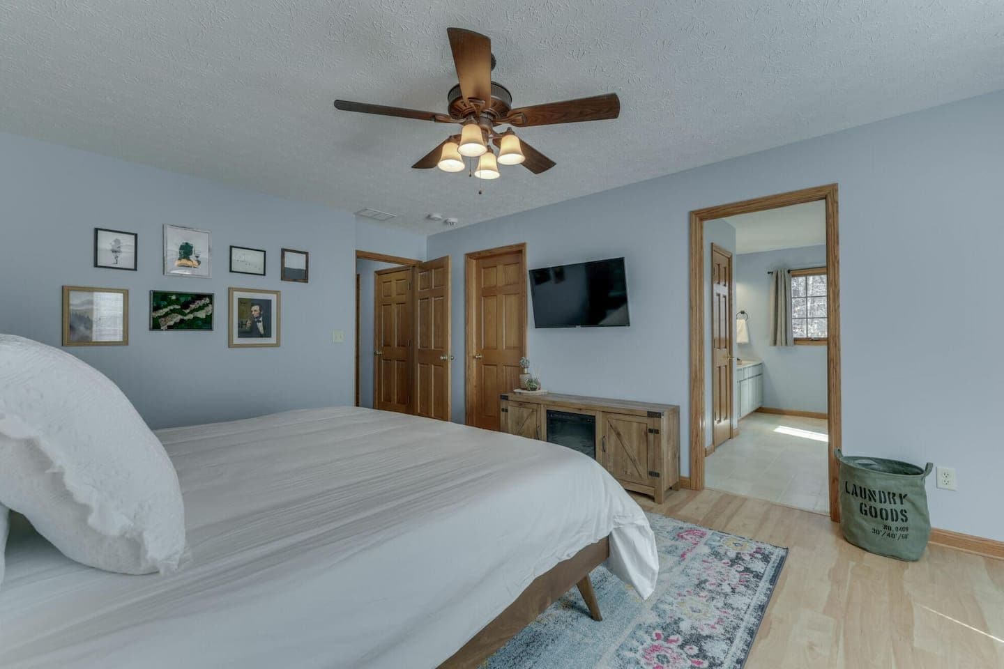 A bedroom with a bed, a ceiling fan, a TV, wooden doors, a mirror, and a laundry basket.