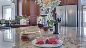 Una cocina con encimeras de granito, una copa de vino, una botella de vino y carne cruda en un plato.