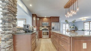 Una cocina con gabinetes de madera, una pared de acento de piedra, electrodomésticos de acero inoxidable e iluminación colgante.