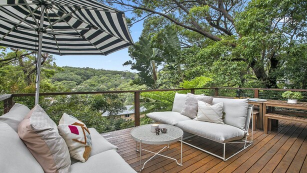 A wooden deck with a white sofa, a round table, and an umbrella.