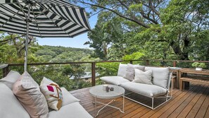 A wooden deck with a white sofa, a round table, and an umbrella.