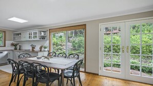 A dining area with a table and chairs, a kitchen with cabinets and a window, and a sliding glass door leading to a garden.