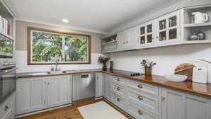 A kitchen with white cabinets, a wooden countertop, a window with a view of greenery, and a white rug.