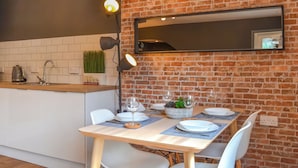 Een moderne keuken met een bakstenen muur, witte kasten en een eethoek met een tafel gedekt voor twee personen.