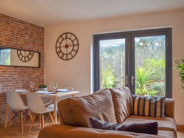 A modern living room with a brick wall, a dining area with chairs and a table, and large windows with a view of greenery. - Lovely annexe adjoining the owner’s property close to the village of Treorchy. (Pentre)