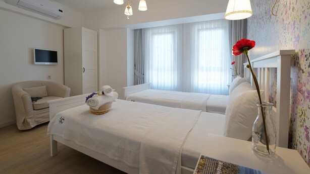 Quarto de hotel com duas camas, televisão, candelabro e um vaso com uma flor.