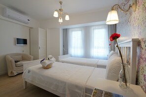 Une chambre d’hôtel avec deux lits, un téléviseur, un lustre et un vase avec une fleur.