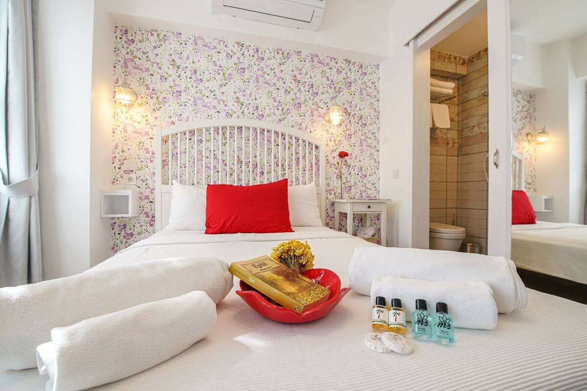 A hotel room with a bed, a red decorative bowl, toiletries, and a bathroom visible through an open door.
