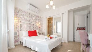 Quarto com cama, mesa de cabeceira, cômoda, cadeira e banheiro visível por uma porta aberta.