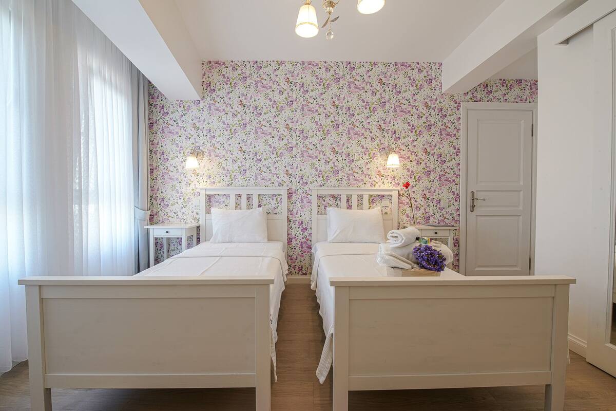 A bedroom with two beds, a white door, and floral wallpaper.