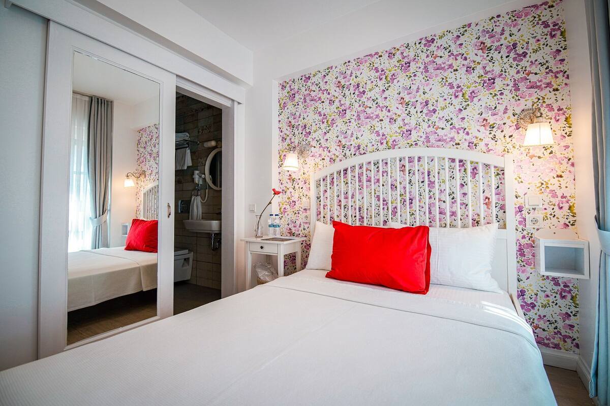 A bedroom with a bed, a nightstand, a mirror, and a wardrobe.