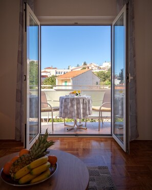 Ein Zimmer mit Holzboden, einem Tisch mit Obstschale und Blick auf einen Balkon mit Tisch und Stühlen.