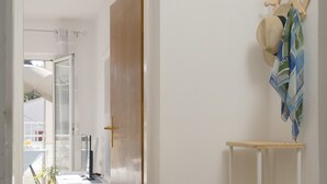 En hall med en vit dörr som leder in till ett rum med ett skrivbord och en stol. Där finns en liten vit hylla med en gul tallrik ovanpå.