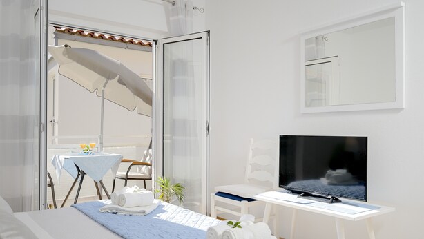 Ett hotellrum med en säng, en TV, ett litet bord med en stol och en balkong med ett bord och stolar.