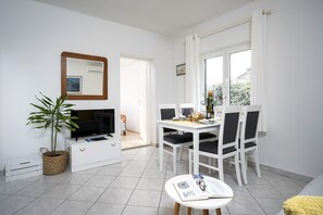 A modern, well-lit room with a dining table set for two, a television, and a potted plant. - One bedroom apartment with terrace (Stari Grad)