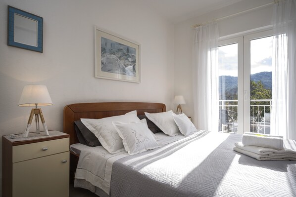 A bedroom with a bed, bedside lamps, a nightstand, a window with a view, and a framed picture on the wall. - One bedroom apartment with terrace (Stari Grad)