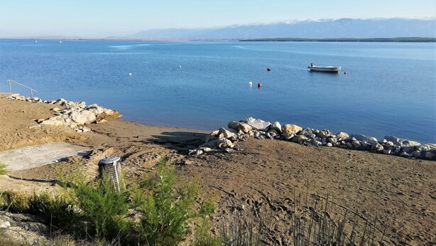 A beach with a rocky shoreline, a boat, and a clear view of distant mountains. - One bedroom apartment with seaview balcony (Nin)