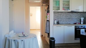 A compact kitchen with a small dining area, a trash bin, and a clock on the wall. - One bedroom apartment with seaview balcony (Nin)
